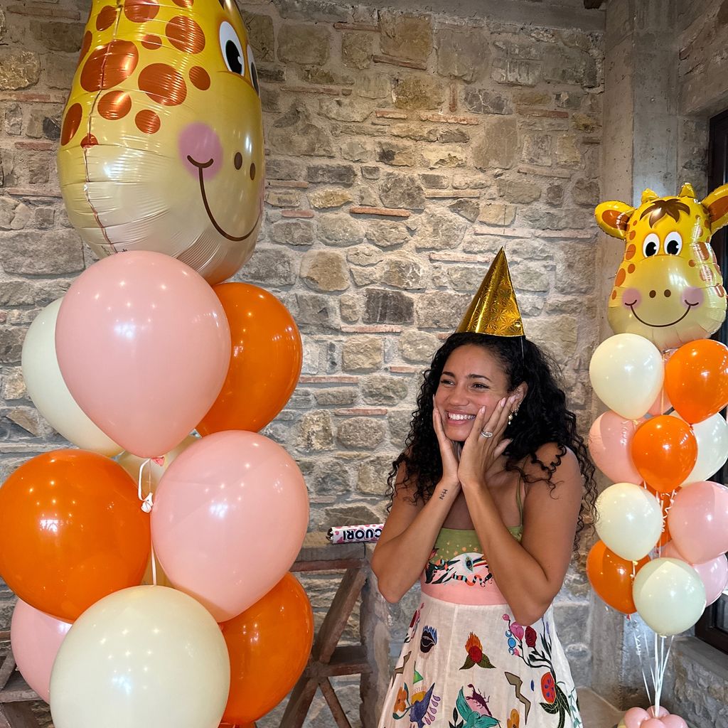 woman wearing gold cone hat surrounded by pink and orange balloons 