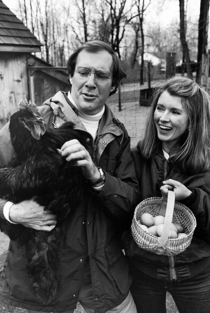 Andrew Stewart holding a black Cochin hen and wife, Martha Stewart, holding a basket of eggs in barnyard of their home, ca. 1980