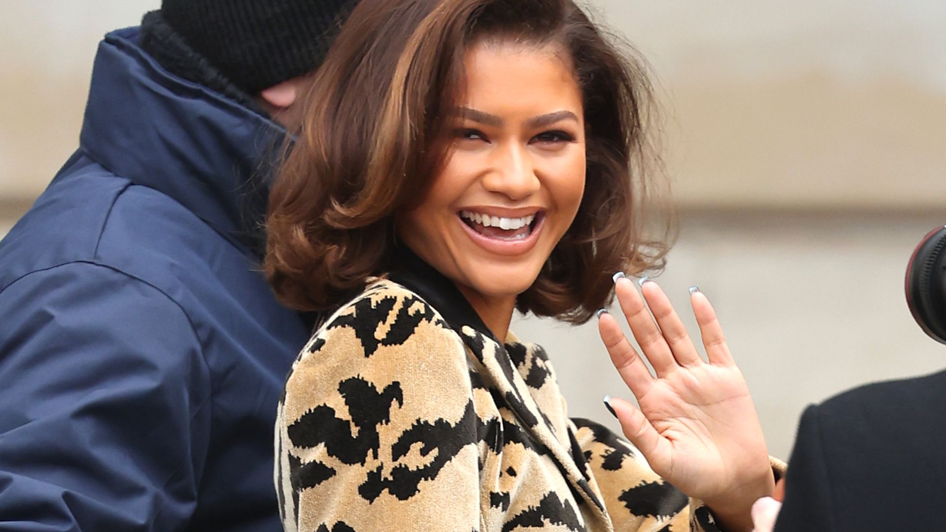 Zendaya attending Paris Fashion Week in 2023 waving at the camera and smiling