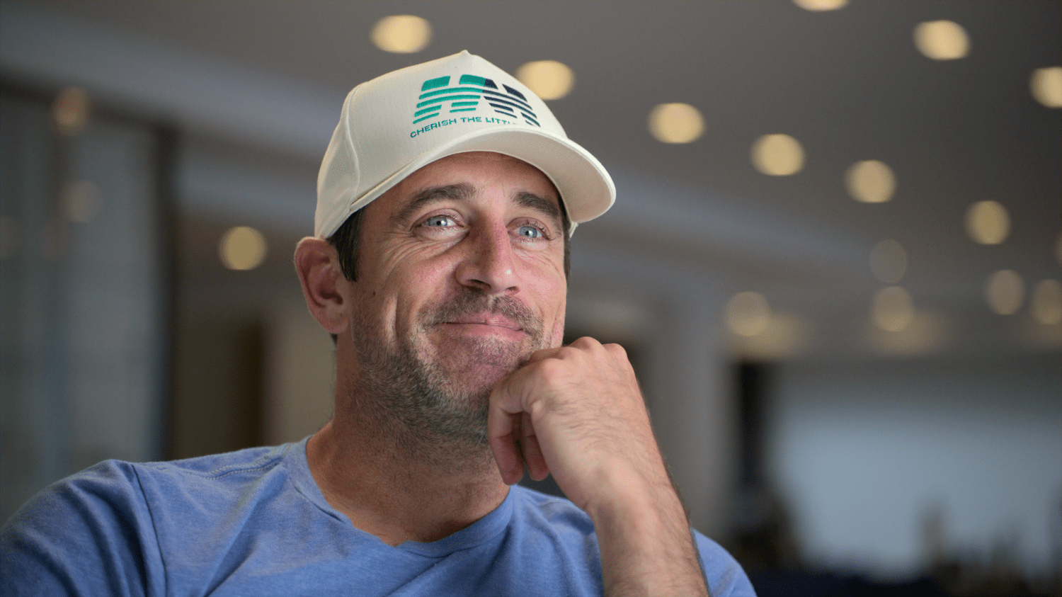 Aaron Rodgers wears a baseball cap and blue t-shirt.