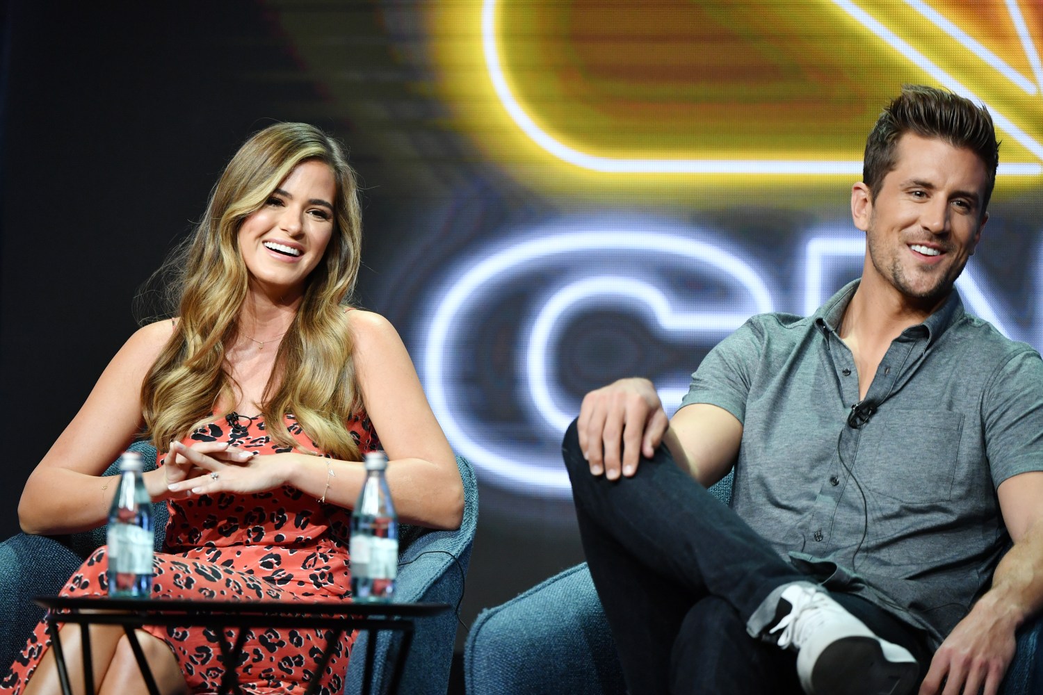 Jordan Rodgers and JoJo Fletcher sit on stage during an event for NBC.