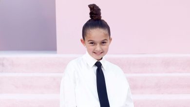 Taylen Biggs poses on the red carpet in a white shirt, black tie and white boots while carrying a black studded mini purse