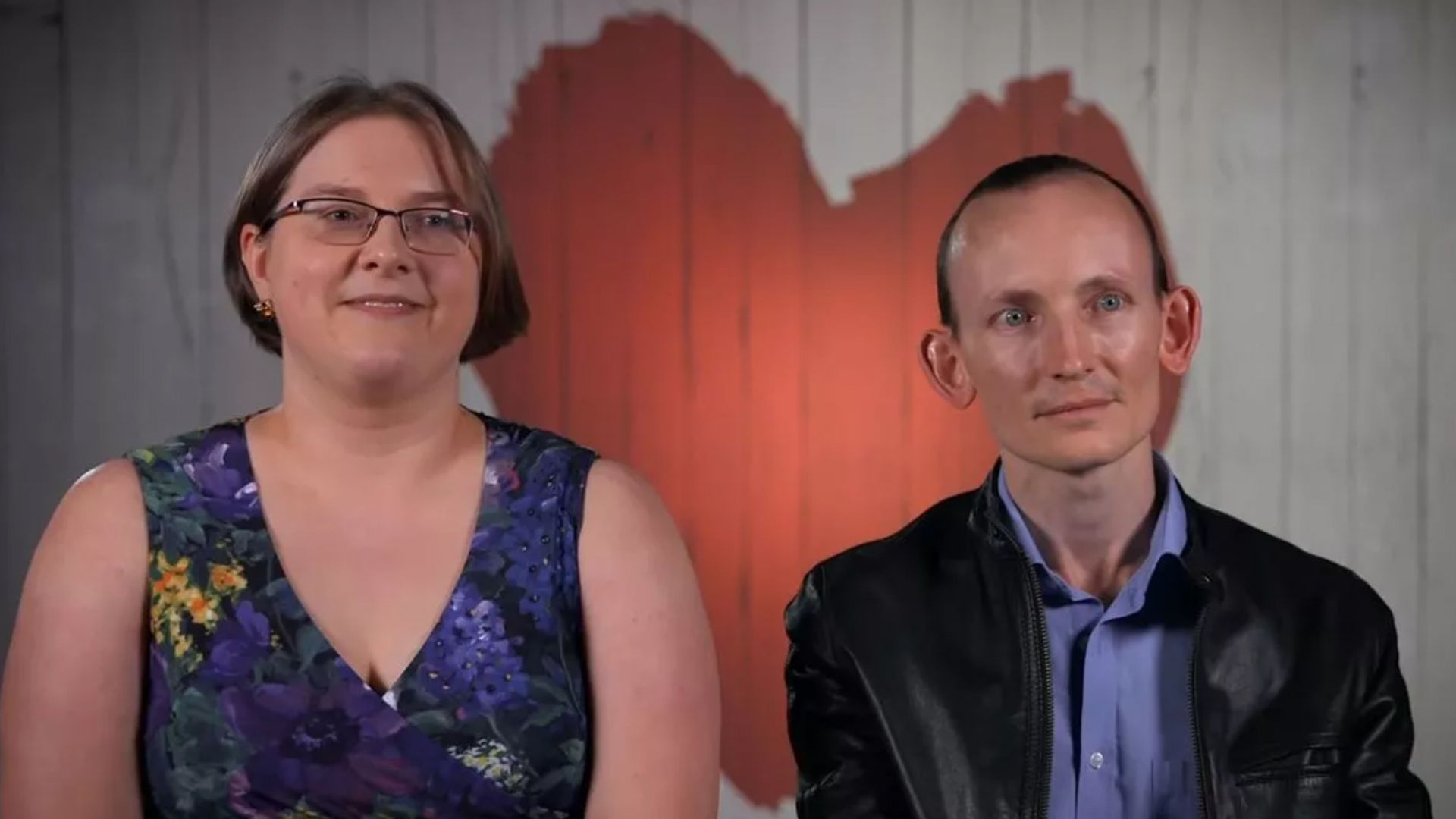 A heterosexual couple sitting in front of a heart