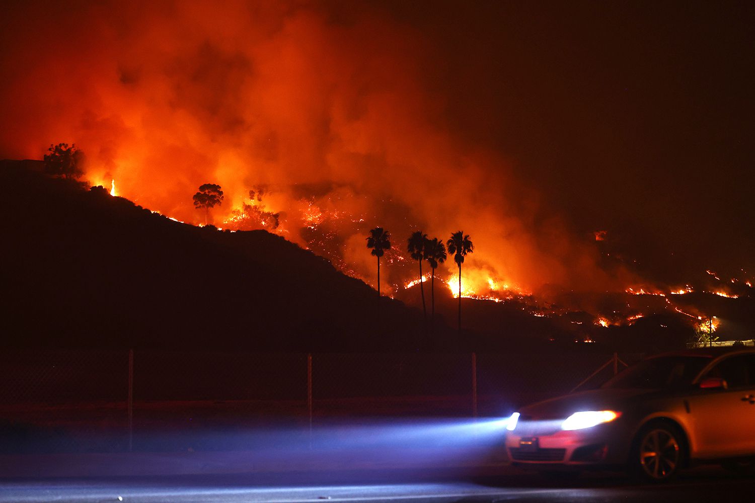 A car drives as the Franklin Fire burns on December 10, 2024 in Malibu, California. The wildfire has scorched 1,800 acres near Pepperdine University prompting evacuations along the coast amid high winds with some structures destroyed. 