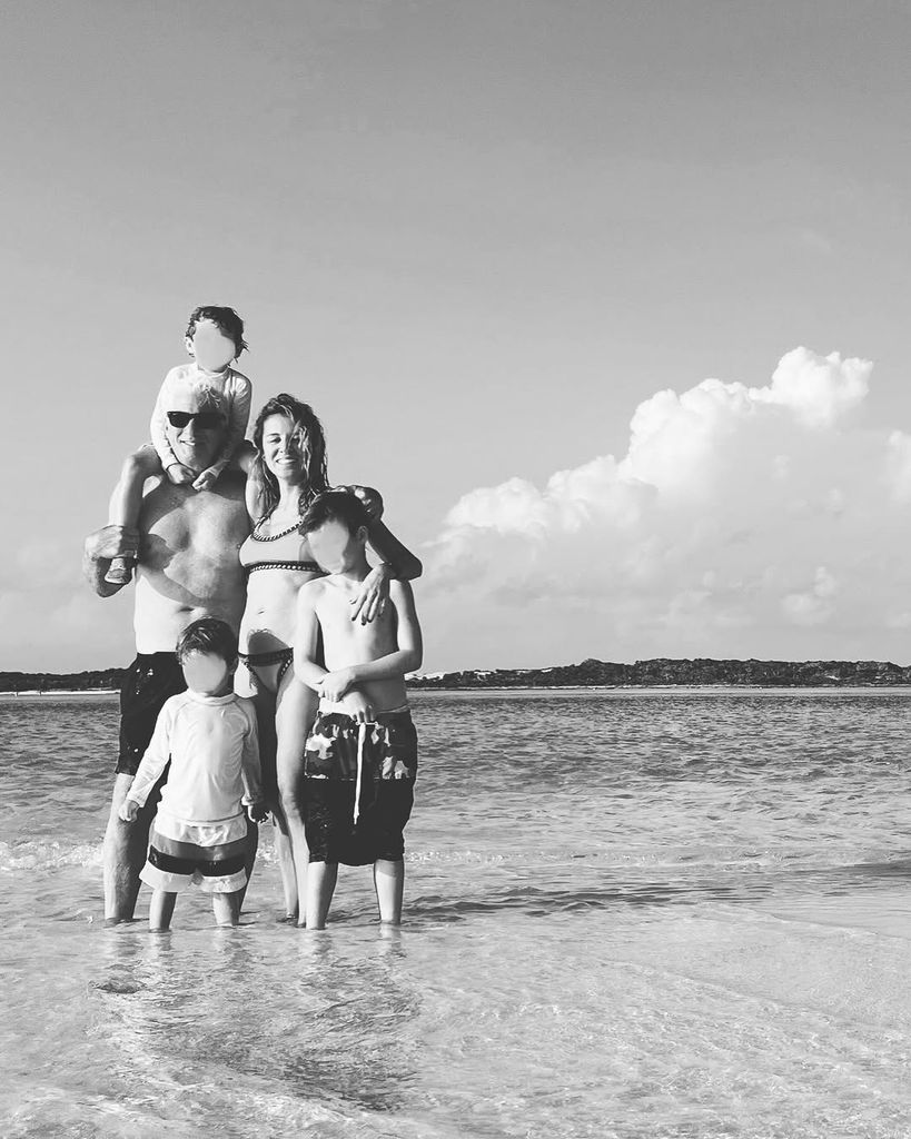 Black and white photo showing Richard, Alejandra and three of their sons standing in the ocean while on vacation