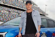 Alan Ritchson poses next to a Daytona 500 car.