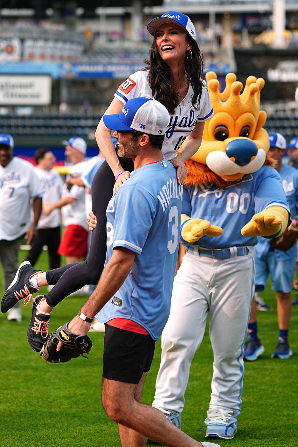 Tyler Hoechlin lifts Bitsie Tulloch in a Celebrity Softball game at Kauffman Stadium during the Big Slick Celebrity Weekend benefiting Children's Mercy Hospital on May 30, 2025 in Kansas City, Missouri. 