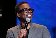 Chris Rock stands on stage holding a microphone.