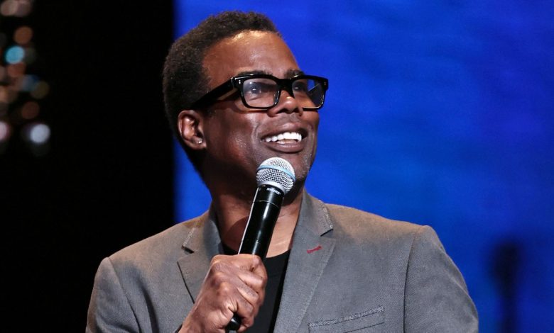 Chris Rock stands on stage holding a microphone.