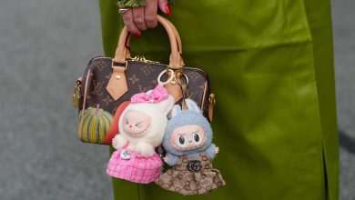 A guest wears a bright olive-green leather coat with a green snake-print cuff peeking from the sleeve, a silver-toned ring, and a glossy red pointed manicure, while a brown Louis Vuitton Monogram coated-canvas mini top-handle bag with tan vachetta leather rolled handles, leather tabs, a gold-tone zipper and padlock, and a yellow-and-orange pumpkin motif is carried; two Labubu plush bag charms are attached-one cream plush figure in a pink tweed dress with a matching bow, the other blue-gray plush with bunny ears in a brown Gucci GG monogram dress finished with a black Double G emblem and gold-tone hardware attachments, outside Rotate, during Copenhagen Fashion Week, on August 07, 2025 in Copenhagen, Denmark